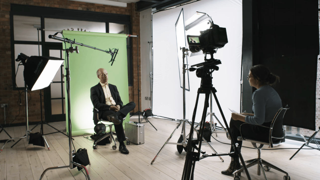Man being interviewed in front of a camera and green screen